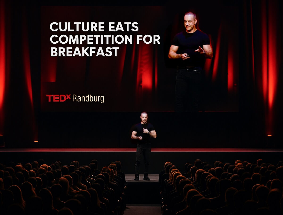 Bryan Adams on the TEDx stage with the slide 'Culture Eats Competition for Breakfast'